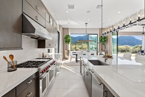 A modern kitchen with a central island, stainless steel appliances, and a view of mountains through large windows. - NEW Luxury|Pool|Spa|Sevens Escape at Sereno Canyon (Scottsdale)