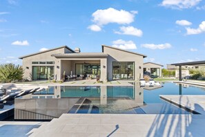 Ein modernes Haus mit Pool, einer Terrasse und Liegestühlen sowie blauem Himmel.