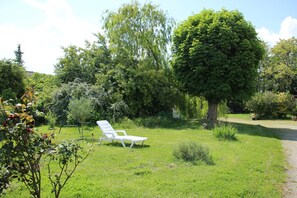 A garden with a white lounge chair, a large tree, and various shrubs. - Gîte des Voines - MAILLE (MAILLE)