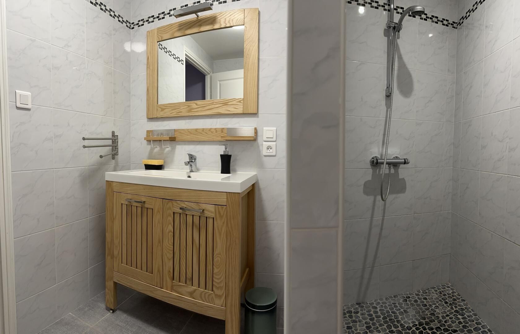 Une salle de bain avec un meuble-lavabo en bois, un miroir, une douche avec un sol carrelé et un mur carrelé.