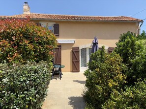 Une maison avec un toit en tuiles, une porte et une fenêtre. Il y a une chaise et une table à l’extérieur.