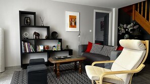A modern living room with a sofa, armchair, coffee table, bookshelf, and artwork. - Gîte des Voines - MAILLE (MAILLE)