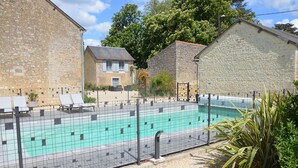 Ein Schwimmbecken mit Umzäunung, umgeben von Steingebäuden und blauem Himmel.