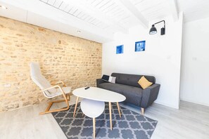 A modern living room with a stone wall, a grey sofa, a white table, and a patterned rug. - Le Gite du Cèdre - MONTAMISE (MONTAMISE)