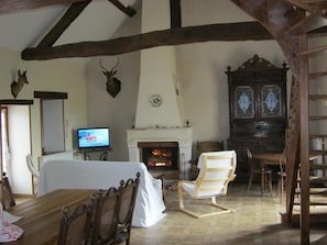 Ein Zimmer mit Kamin, Holzbalken, Fernseher und einem Esstisch mit Stühlen.