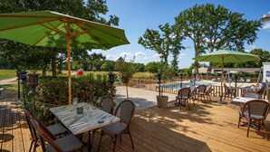 Una terraza de madera con mobiliario exterior, una piscina y vistas del paisaje circundante.