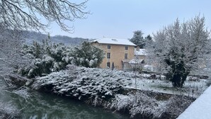 A building with a traditional architectural style, a body of water in the foreground, and snow-covered trees.