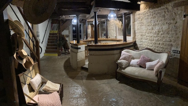 A rustic interior with a stone wall, a wooden staircase, a round wooden table, and a white sofa with pink cushions.