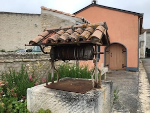 An outdoor mechanical device with a metal roof, possibly a historical artifact, situated on a stone base with a wall and a building in the background. - La Blanche Maille - CISSE (CISSE)