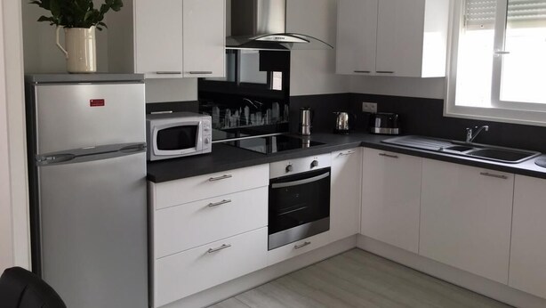 Eine moderne Küche mit weißen Schränken, einer Edelstahl-Dunstabzugshaube, einer Mikrowelle, einem Backofen und einem Spülbecken.
