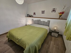A bedroom with a bed, nightstands, a wall-mounted shelf with books, decorative items, and a hanging light fixture. - La Blanche Maille - CISSE (CISSE)