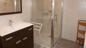 Un bagno con cabina doccia in vetro, un lavandino con specchio e una mensola in legno.