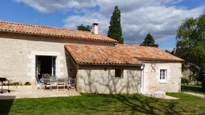 Un edificio in pietra con tetto in tegole, un patio con tavolo e sedie, e un prato.