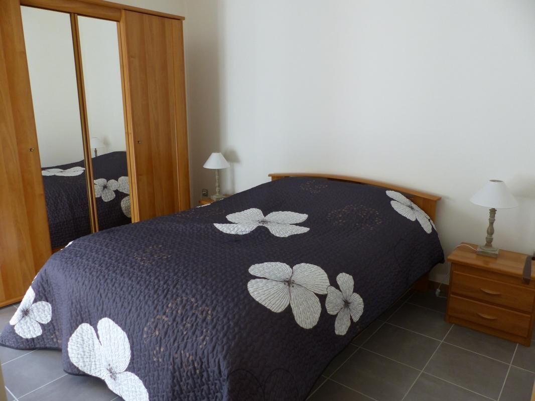 A bedroom with a bed, a wardrobe, a nightstand, and a lamp.