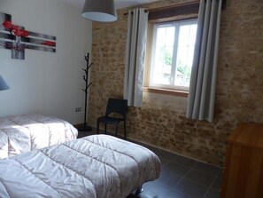 Ein Schlafzimmer mit zwei Betten, einem Fenster mit Vorhängen, einem Sessel und einer Lampe.