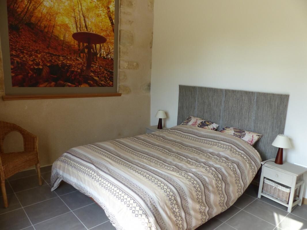A bedroom with a bed, two bedside tables, a lamp, a chair, and a painting on the wall.