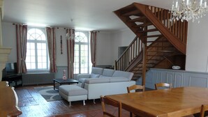 Un salon comprenant un canapé, un pouf, une table à manger en bois, des chaises, un escalier et un téléviseur.