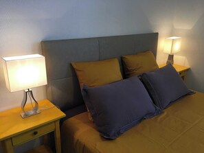 Een bed met twee kussens, twee nachtlampjes en een nachtkastje met een lade.