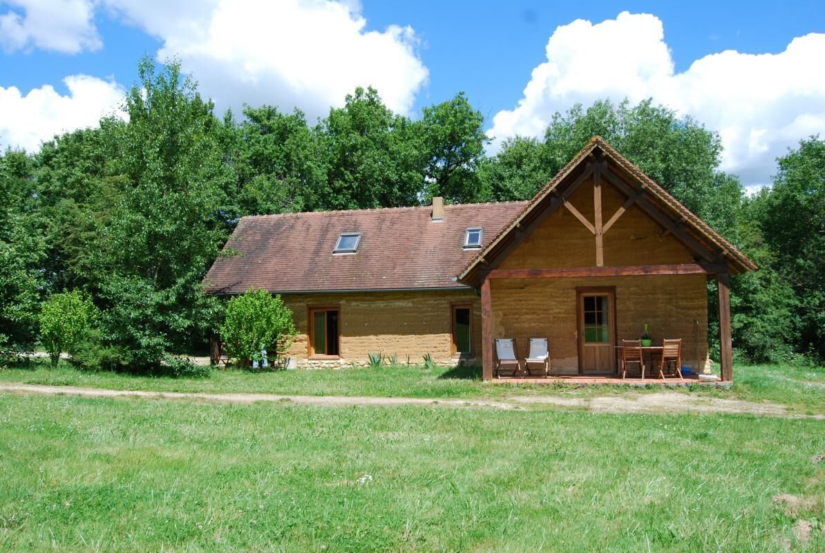 A rustic wooden house with a sloped roof, a porch with two chairs and a table, and a small window.