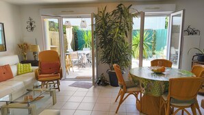 Un soggiorno con divano, poltrone, un tavolino in vetro, un tavolo da pranzo con sedie, una grande pianta in vaso e una porta scorrevole in vetro che dà su una zona esterna.