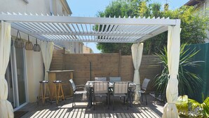 Una veranda riparata con tavolo e sedie, uno sgabello e un recinto in legno.