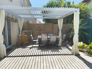 A covered patio with a table and chairs, a small stool, and a wooden fence. - La Royannaise" house by the sea (Royan)