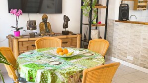Zona pranzo con un tavolo rotondo, sedie in vimini, una statua di Buddha, un televisore e una mensola per piante.