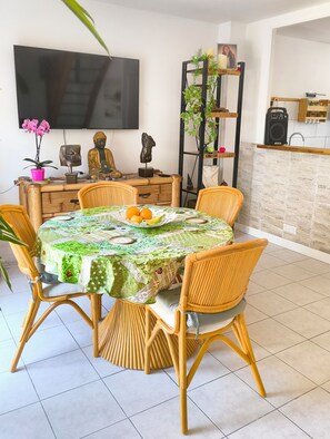 A dining area with a round table, wicker chairs, a Buddha statue, a TV, and a plant shelf. - La Royannaise" house by the sea (Royan)