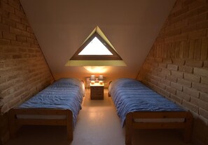 A small attic bedroom with two single beds, a nightstand, and a skylight.