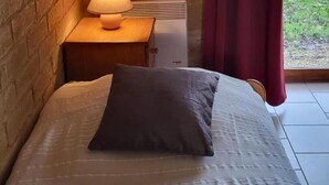 Un dormitorio con pared de ladrillo, una mesita de noche con lámpara, una cama con almohada y una ventana con cortinas.