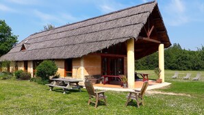 Ein rustikales Reetdachhaus mit einer Holzveranda, einem Picknicktisch und Gartenmöbeln.