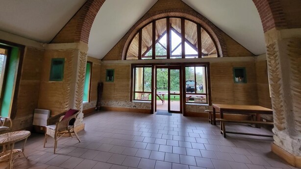 Ein geräumiger Saal mit hoher Rundbogenzwillingsdecke, großen Fenstern und Blick ins Freie.