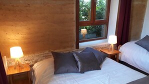 Un dormitorio con dos camas, mesitas de noche de madera, lámparas de noche y una ventana con vistas a zonas verdes, además de una pared de piedra.