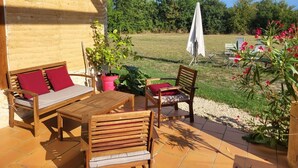 Eine Terrasse im Freien mit Holzmöbeln, einer Ziegelwand und einer Rasenfläche mit Bäumen und einem weißen Sonnenschirm.