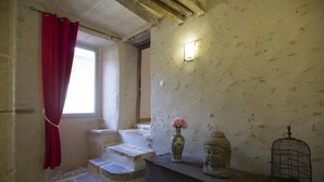 Una habitación con ventana, una cortina roja, un jarrón con flores, una estatua de Buda y una jaula de pájaros.