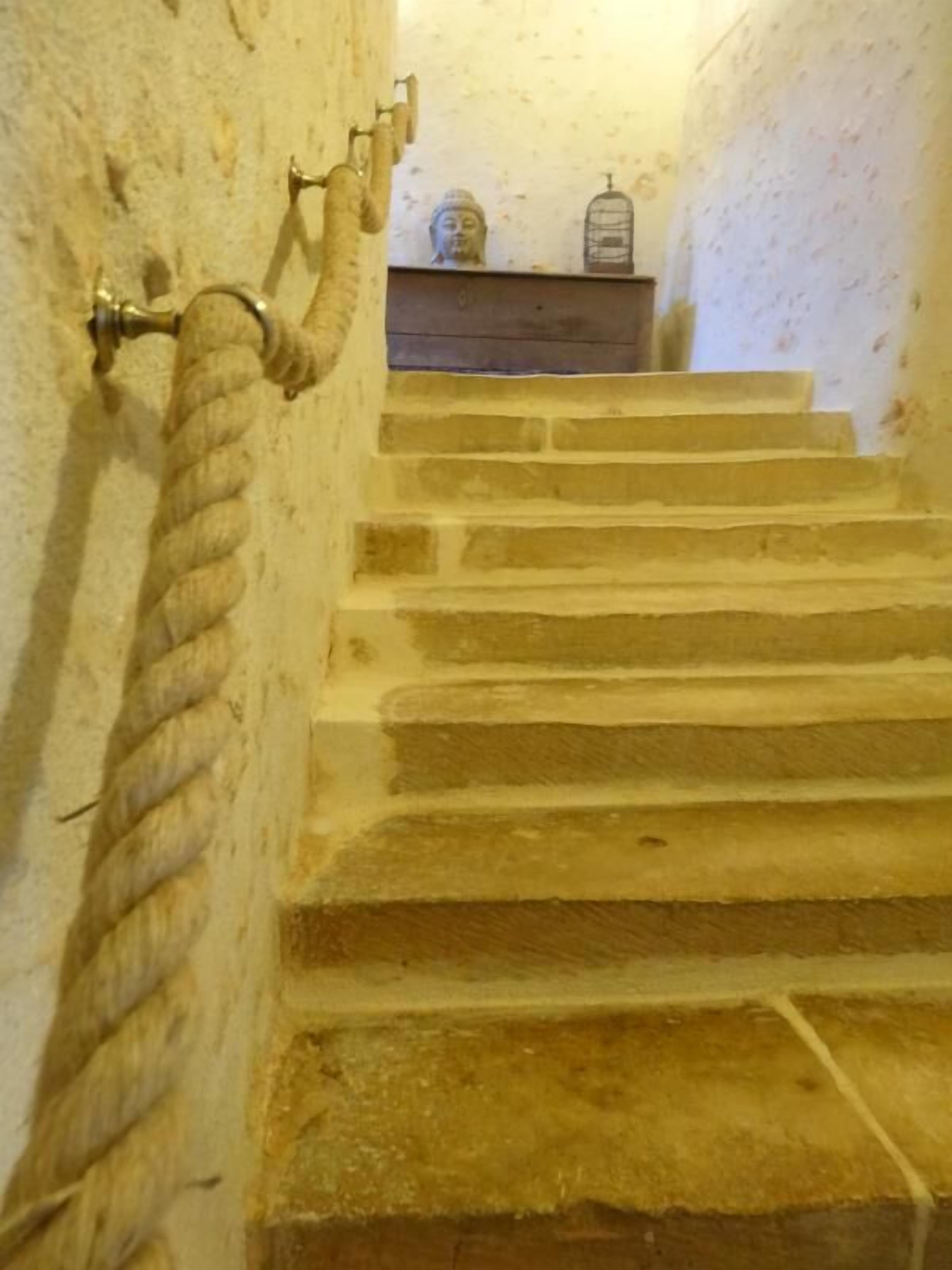 Una escalera de piedra con barandilla de cuerda, una pequeña estatua de Buda y una jaula de pájaros en un estante.