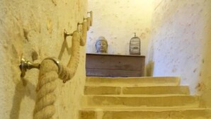 Una escalera de piedra con barandilla de cuerda, una pequeña estatua de Buda y una jaula de pájaros en un estante.