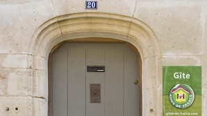 Edificio de piedra con puerta gris, un letrero con el número '20' sobre la puerta y un cartel verde que indica 'Gîte' y una dirección web.