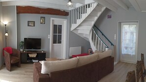 Una sala de estar con un sofá marrón, televisor, escalera y una puerta con ventanal.
