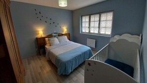 Un dormitorio con cama, lámparas de noche, una ventana con cortinas de encaje, una lámpara de techo y una cuna.