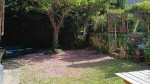Un patio trasero con una mesa de madera, un árbol y un muro de piedra.