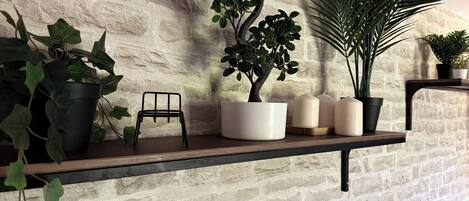 A shelf with potted plants, candles, and a small metal stool against a textured wall.