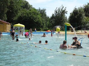 Ein Schwimmbecken mit mehreren Bahnen, einem Wasserspielbereich und einer überdachten Sitzgelegenheit.