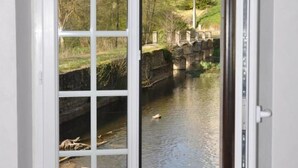A white door with a glass panel, a view of a river, a stone bridge, and buildings in the background. - Le Moulin Brûlé - BETHINES (BETHINES)