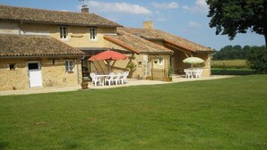 A stone building with a tiled roof, outdoor seating, and a grassy lawn. - The Gallinaceans - LUSIGNAN (LUSIGNAN)
