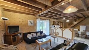 A rustic interior with exposed wooden beams, a sofa, a dining table, a TV, and a kitchen area. - The Gallinaceans - LUSIGNAN (LUSIGNAN)