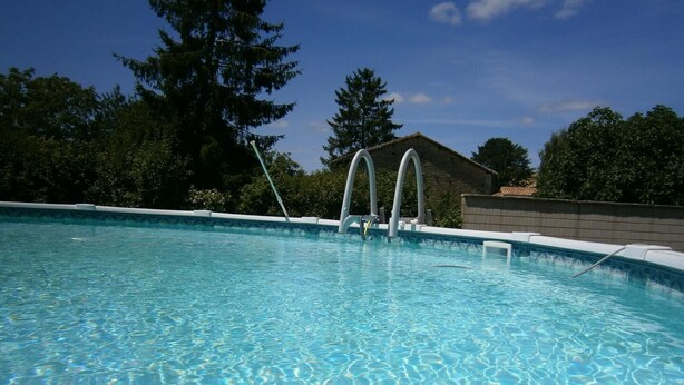A swimming pool with clear water, surrounded by trees and a building in the background. - Les Cèdres - BLANZAY - Gîte (BLANZAY)
