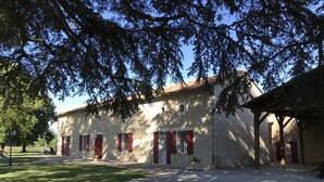 A building with a gravel driveway, red shutters, and a covered area to the right. - Les Cèdres - BLANZAY - Gîte (BLANZAY)