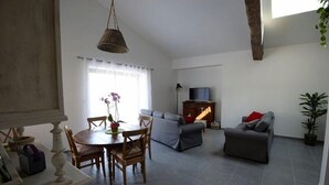 Una sala de estar con una mesa de comedor, sillas, un sofá, un televisor y una planta.