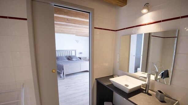 Un baño moderno con un espejo grande, un lavabo y una puerta que da a un dormitorio.